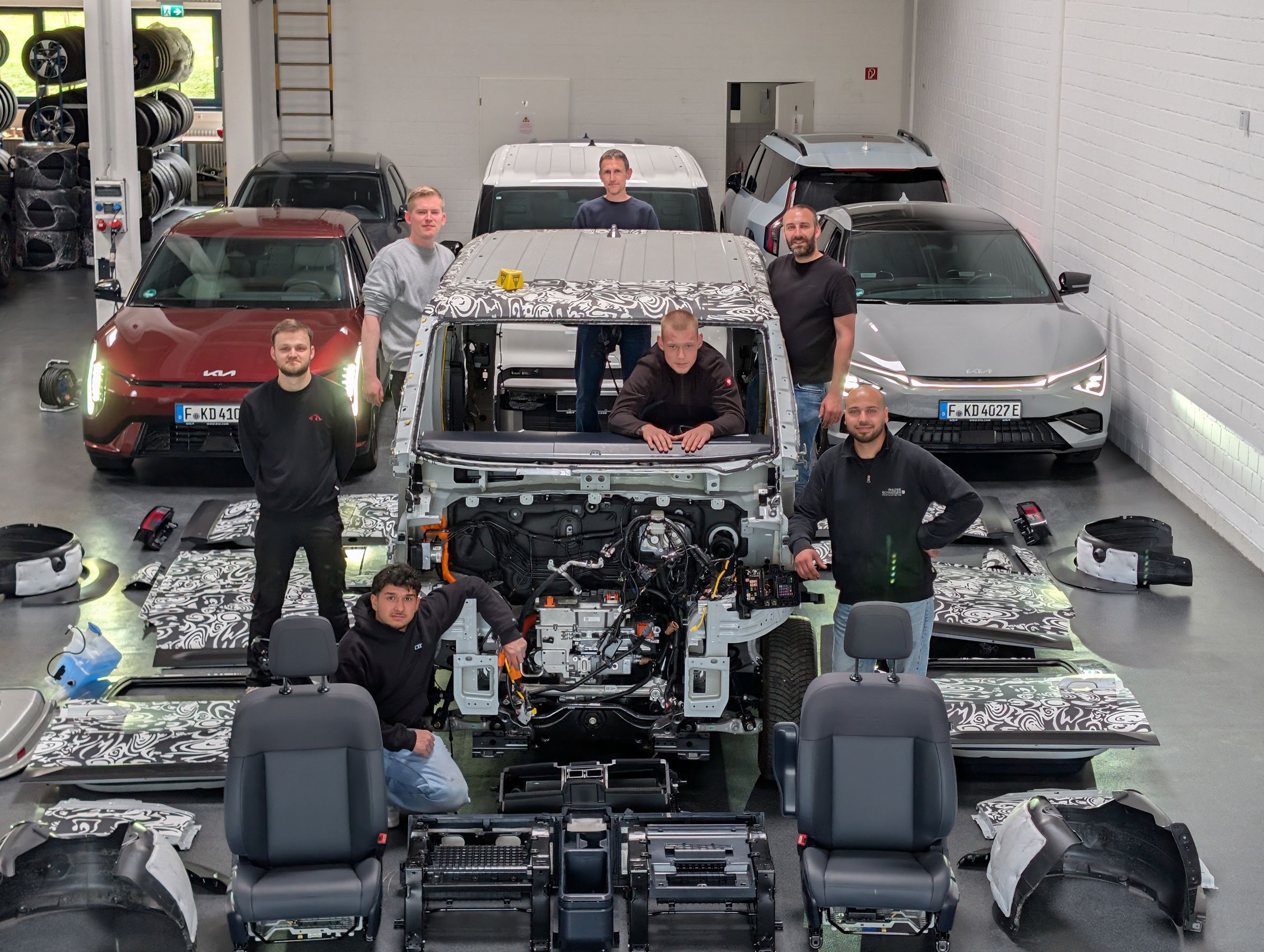 Sechs Mechatroniker bei der Demontage eines Kia PV5 Cargo im Technikzentrum