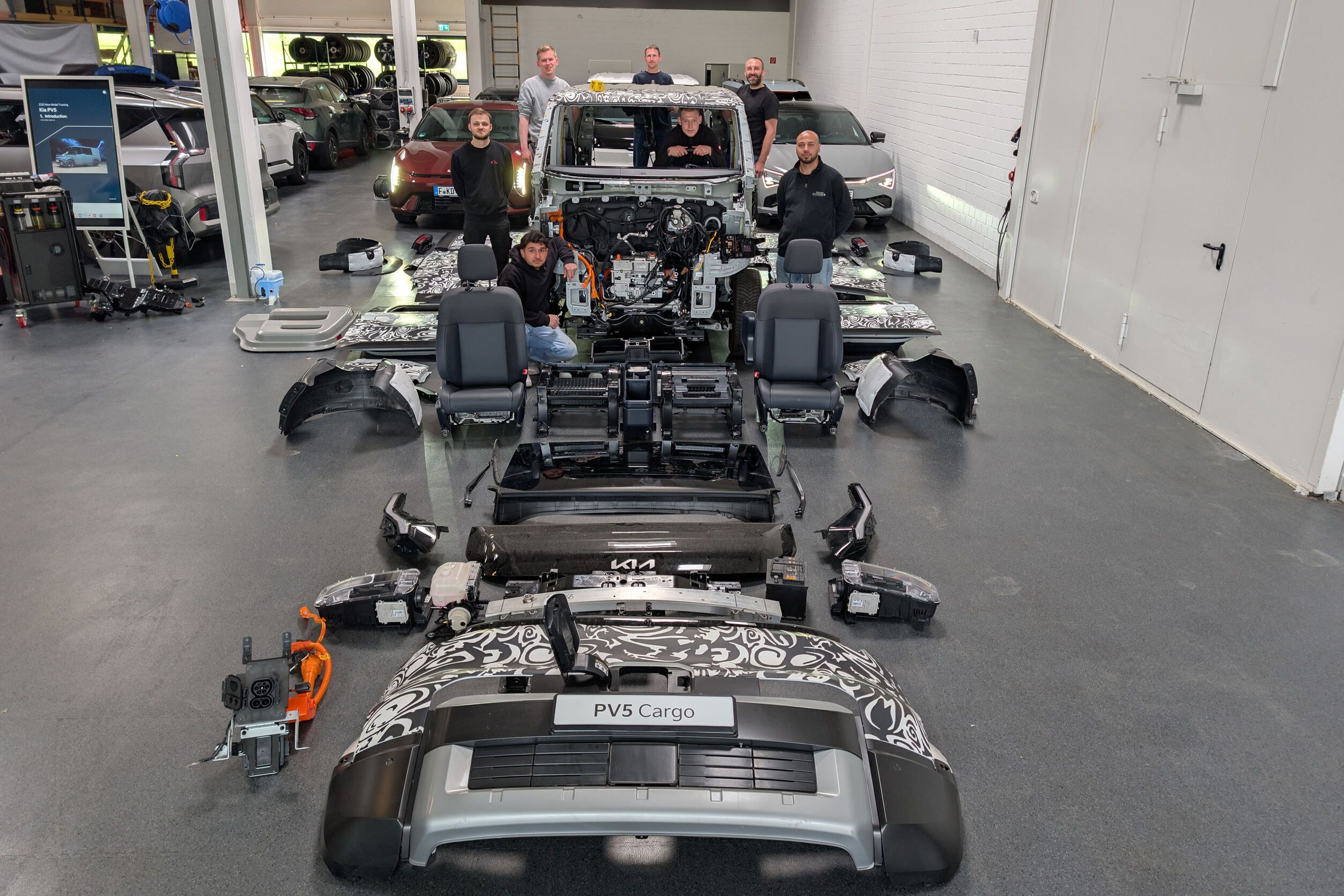 Sechs Mechatroniker bei der Demontage eines Kia PV5 Cargo im Technikzentrum